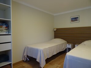 Habitación pequeña con una cama individual, cabecera de madera, mesita de noche y un armario con ropa doblada.