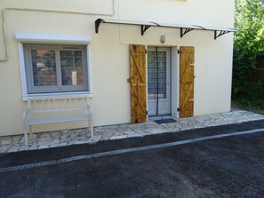 A building with a white window, a door with wooden shutters, and a small bench outside. - Charming, detached garden-level vacation rental near the town center (Neuvic)