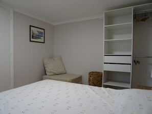 A bedroom with a bed, a wardrobe, a small table, a wicker basket, and a framed picture on the wall.