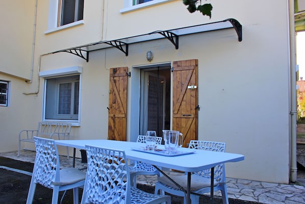 An outdoor seating area with a table and chairs, a wooden door, and a window.