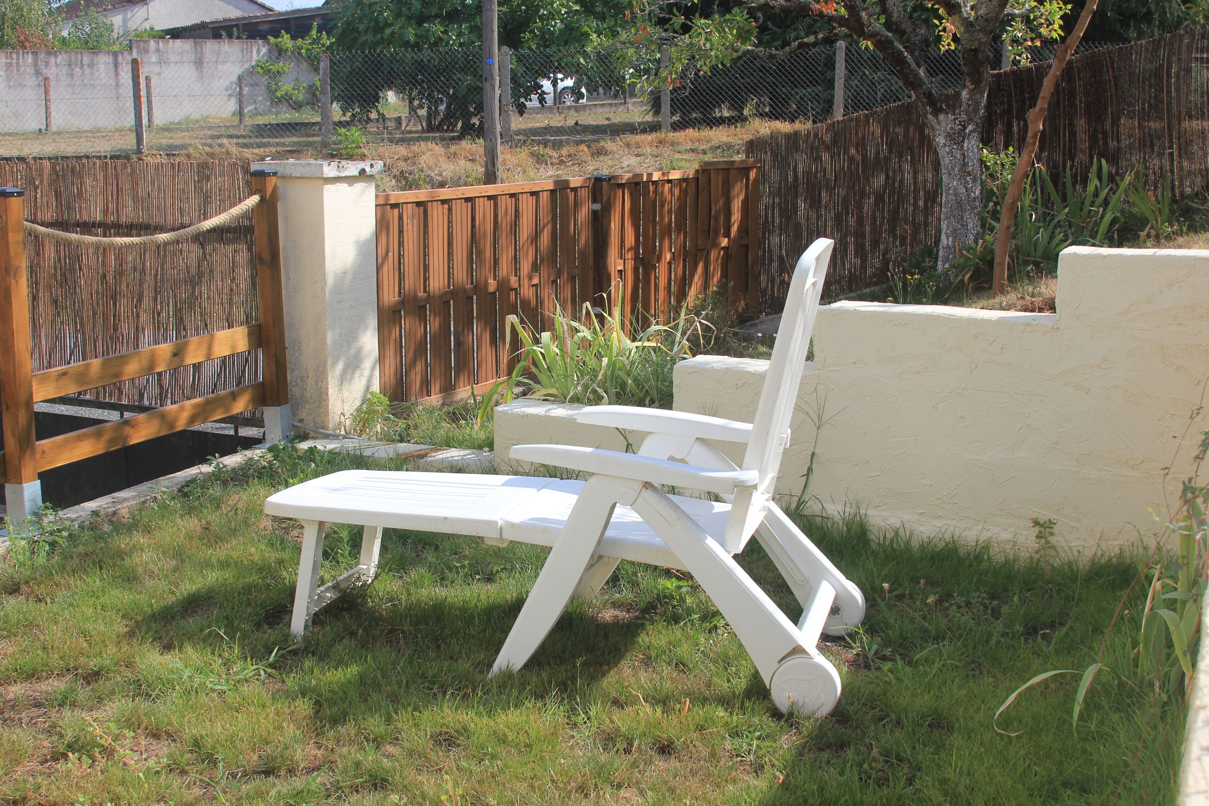 A white lounge chair in a grassy backyard with a wooden fence and a concrete wall.
