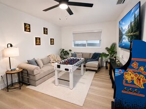 Ein Wohnzimmer mit einem Kicker, einer Couch, einem Couchtisch, einer Lampe und einem Fernseher.