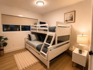 Une chambre avec un lit superposé, une table de chevet, une lampe et un tableau encadré au mur.