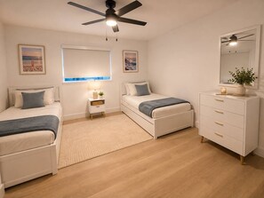 Ein Schlafzimmer mit zwei Betten, einem Nachttisch mit Lampe, einem Schminktisch und einem Deckenventilator.