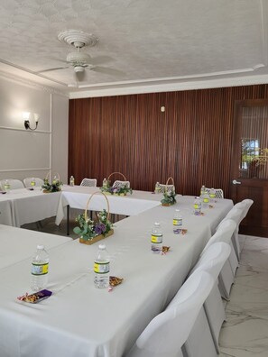 A conference room with long tables, white tablecloths, water bottles, and floral centerpieces. - JamGolia Place (Mandeville)