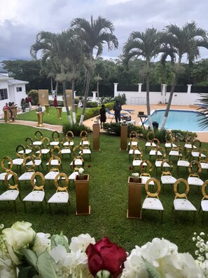 Montaje para una boda al aire libre con filas de sillas y una piscina al fondo.