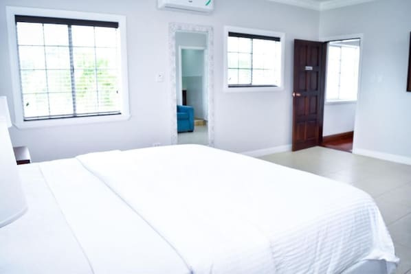 Un dormitorio con una cama grande, dos ventanas y una puerta que da a otra habitación.