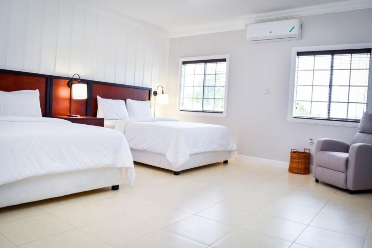Una habitación de hotel con dos camas, una mesita de noche, una lámpara, una silla y una ventana.