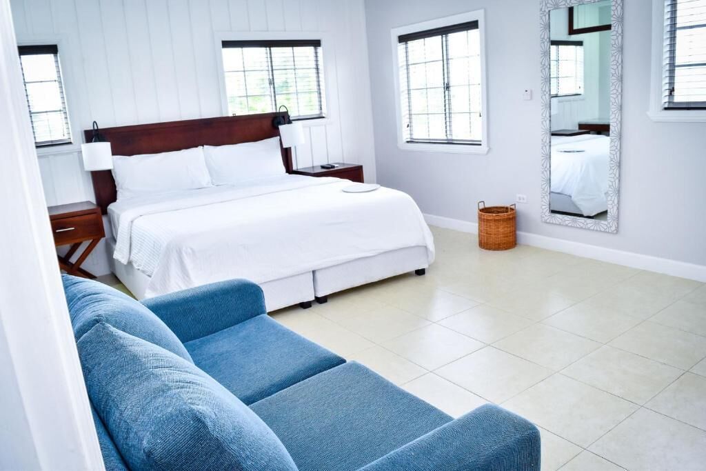 A bedroom with a bed, a nightstand, a bedside table, a blue sofa, a window, and a wall-mounted mirror.