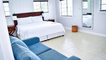 A bedroom with a bed, a nightstand, a bedside table, a blue sofa, a window, and a wall-mounted mirror.
