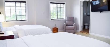 A hotel room with two beds, a television, a chair, and a window.