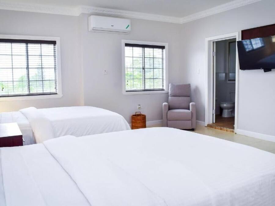 A hotel room with two beds, a TV, a chair, and a window.