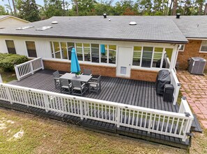 A covered deck with a table and chairs, a grill, and a white railing. - Video Game Hub, Hot Tub, PS5, Xbox, Switch, Pool Table, Air Hockey, Fire Pit (Valdosta)