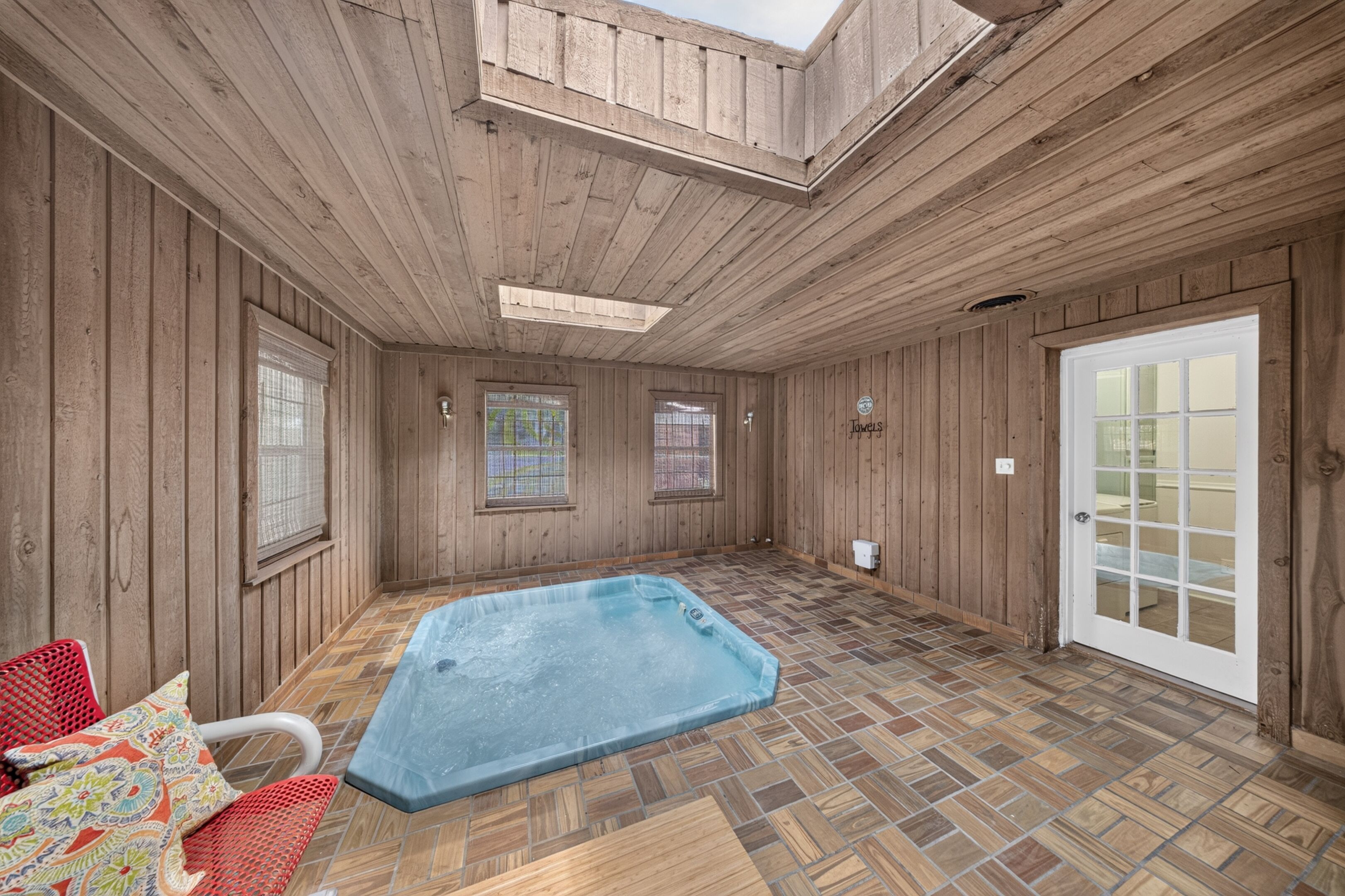 A room with wooden walls, a tiled floor, a hot tub, and a skylight.