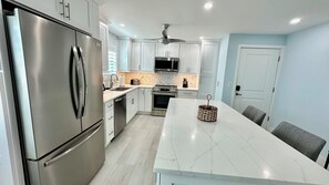 A modern kitchen with stainless steel appliances, a marble countertop, and a ceiling fan. - Tarpon Beach 108: Panoramic water views, 2nd floor, west corner - Sunsets! (Sanibel)