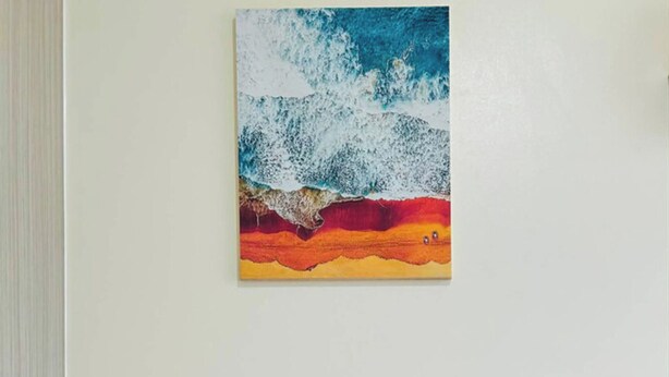 Une pièce avec un seul fauteuil orange, un coussin, une petite table sur laquelle se trouve une boîte de mouchoirs, et un tableau représentant une vague accroché au mur.