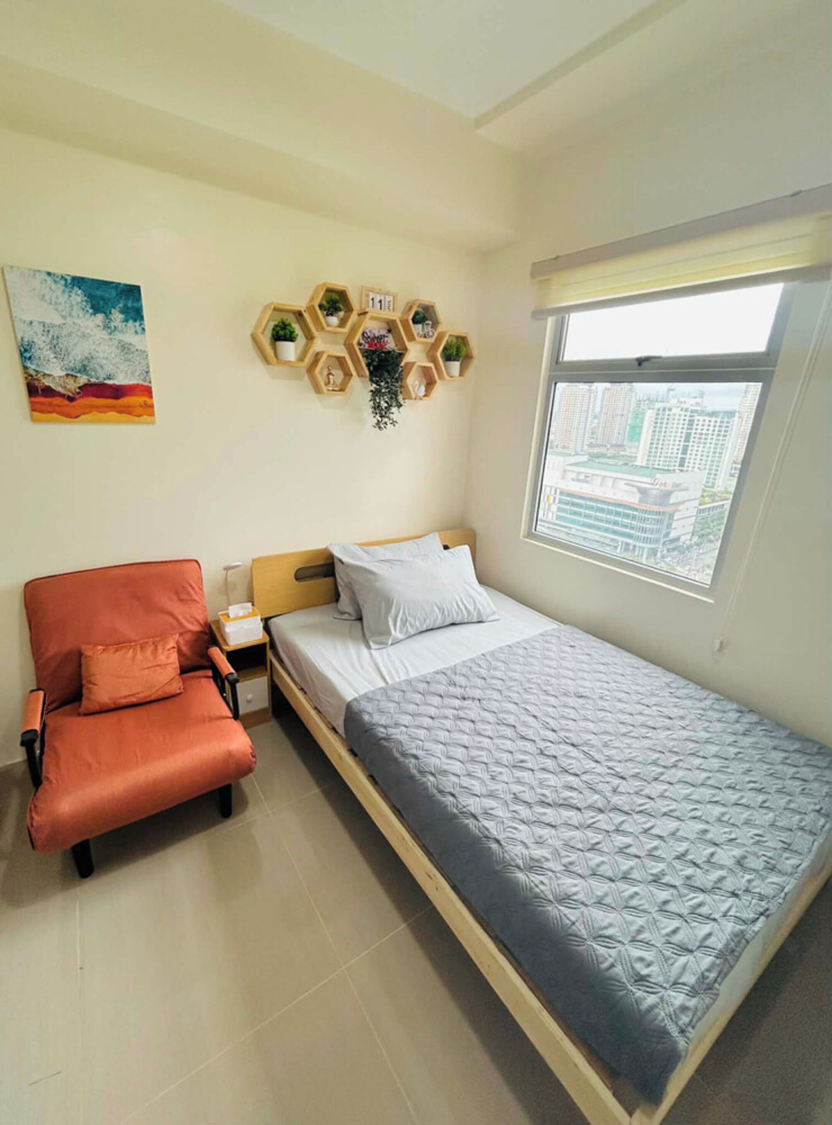 A bedroom with a bed, a chair, a nightstand, a wall clock, a window, and a painting.