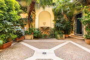 Ein Innenhof mit einem zentralen Brunnen, umgeben von Kübelpflanzen und einem Kopfsteinpflasterboden.