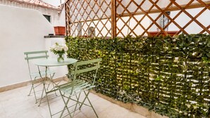 A small outdoor seating area with a table and chairs, a decorative wall with foliage, and a wooden lattice structure. - Elegantis Campo Marzio Apartment With Terrace | Spanish Steps, Trevi & Pantheon (Roma)