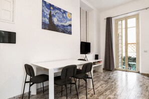 Ein Zimmer mit weißem Schreibtisch, zwei Stühlen, einem Fernseher und einem Bild an der Wand.