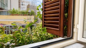 A window with wooden shutters partially open, revealing a view of a balcony with plants and a cityscape in the background. - Elegantis Campo Marzio Apartment With Terrace | Spanish Steps, Trevi & Pantheon (Roma)