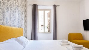 A hotel room with a bed, a window with curtains, a television mounted on the wall, and a chair. - Elegantis Campo Marzio Apartment With Terrace | Spanish Steps, Trevi & Pantheon (Roma)