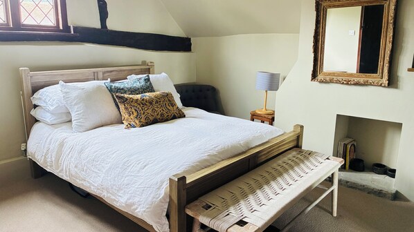 A bedroom with a wooden bed, multiple pillows, a bench, a bedside table with a lamp, and a mirror on the wall.