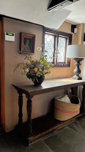 A room with a wooden console table, a vase of flowers, a framed picture, a lamp, and a window with a view.