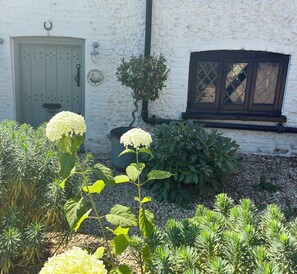 A white building with a green door, a window with diamond panes, and a sign that reads 'COTTAGE.'