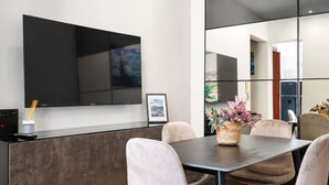 Ett modernt matområde med en platt-TV som är monterad på väggen, ett mörkt träbord och bekväma stolar med vaddering.