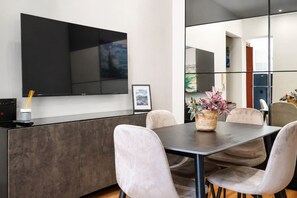 A modern dining area with a flat-screen TV mounted on the wall, a dark wooden table, and cushioned chairs. - Elegantis Campo Marzio Penthouse With Terrace | Spanish Steps, Trevi & Pantheon (Roma)
