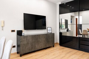A modern living room with a flat-screen TV mounted on a grey cabinet, a large mirror reflecting the room, and a wooden floor. - Elegantis Campo Marzio Penthouse With Terrace | Spanish Steps, Trevi & Pantheon (Roma)