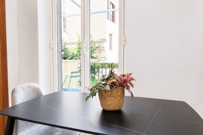 Una habitación con una mesa de madera oscura, una cesta tejida con plantas y vistas a un balcón con barandilla y follaje.