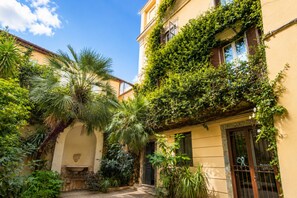 A courtyard with a palm tree, a fountain, and a building with a balcony covered in greenery. - Elegantis Campo Marzio Penthouse With Terrace | Spanish Steps, Trevi & Pantheon (Roma)