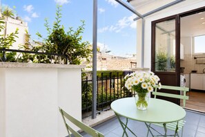 A balcony with a table and chairs, a vase of flowers, and a view of buildings and trees. - Elegantis Campo Marzio Penthouse With Terrace | Spanish Steps, Trevi & Pantheon (Roma)