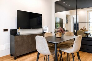 A modern dining area with a flat-screen TV mounted on the wall, a dark wooden dining table, and light-colored chairs. - Elegantis Campo Marzio Penthouse With Terrace | Spanish Steps, Trevi & Pantheon (Roma)