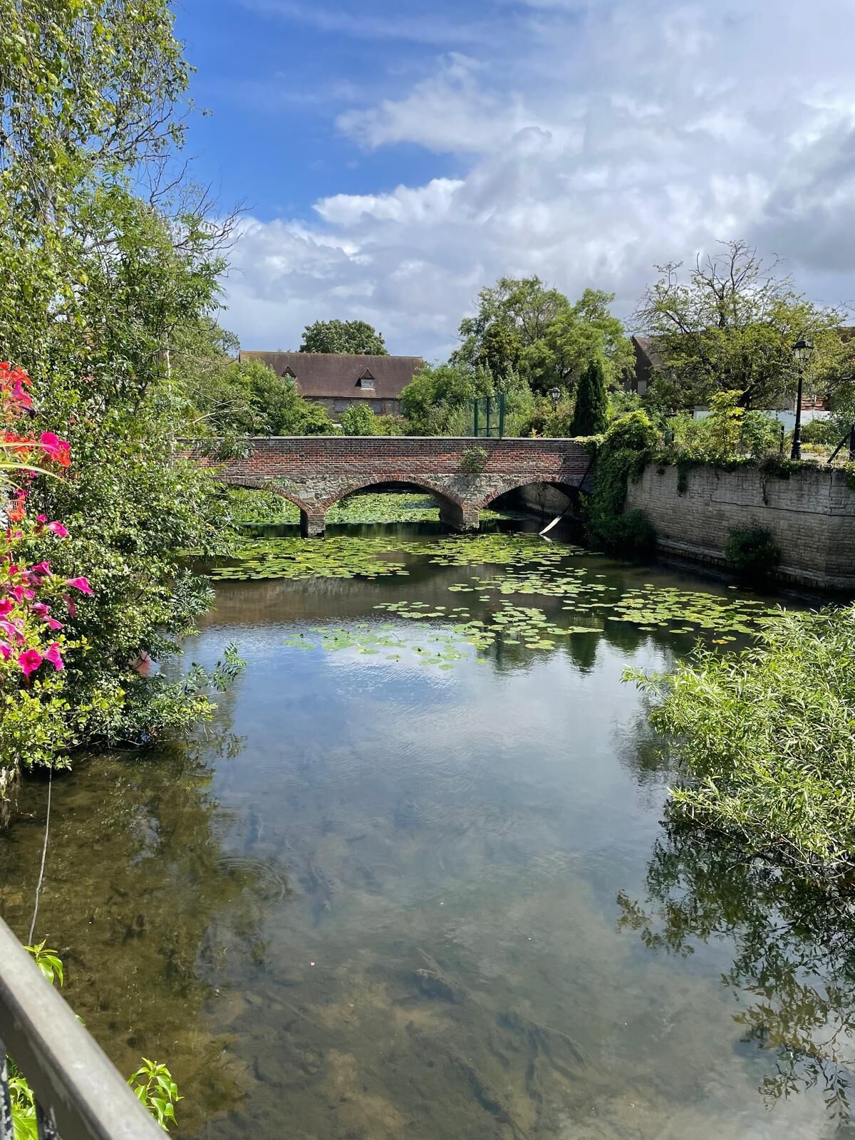 Un paysage paisible au bord de la rivière, avec un pont de pierre, une végétation luxuriante et un ciel dégagé.