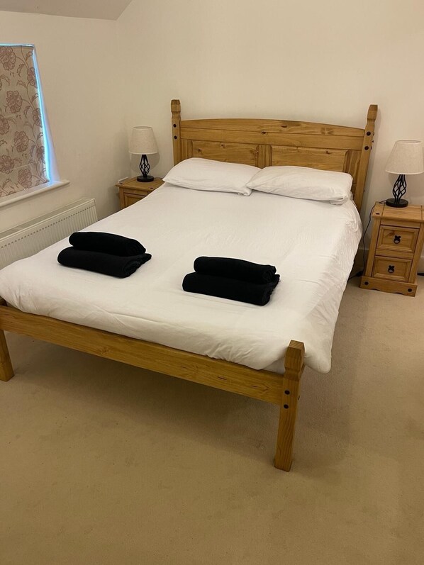 A wooden bed with white bedding, two bedside tables with lamps, and a window with floral curtains.