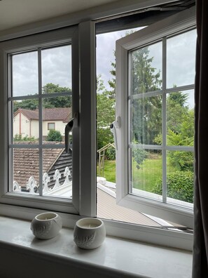 A room with a large window, two small white candle holders on the windowsill, and a view of a house and greenery outside.