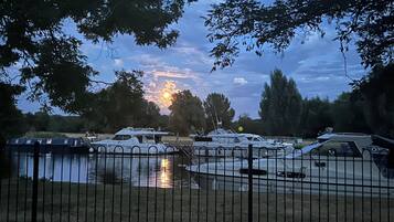 Un puerto deportivo con barcos amarrados, una cerca al frente y árboles al fondo.