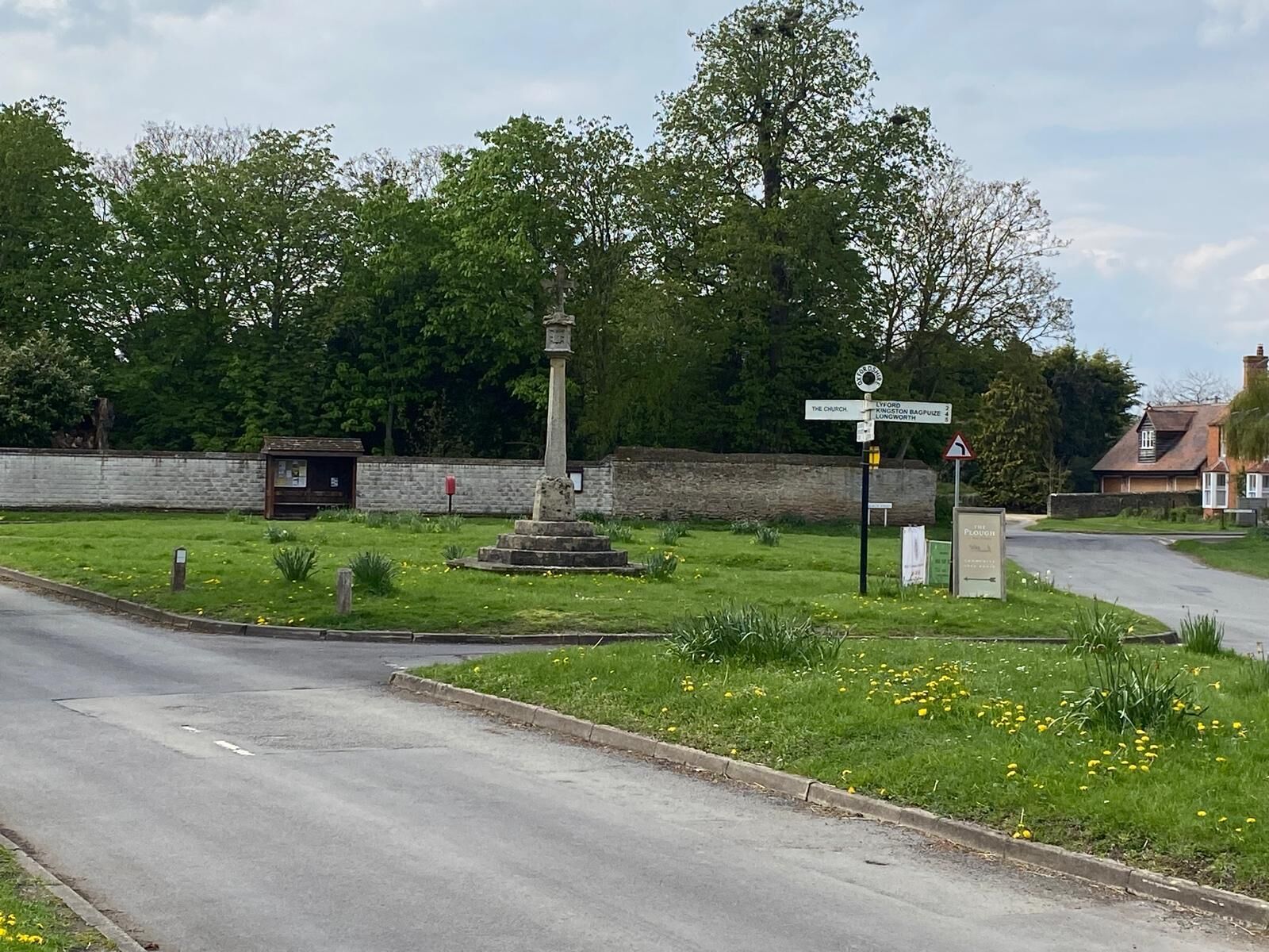 Een landweg met een richtingwijzer, een stenen monument en een grasveld met bloemen.