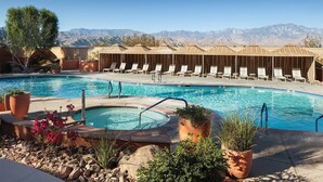 Ein Pool mit Liegestühlen und einem Whirlpool, umgeben von Topfpflanzen und einer Bergkulisse.