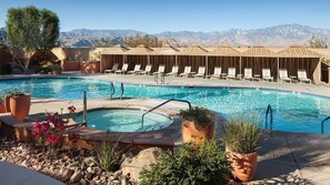 Ein Pool mit Liegestühlen und einem Whirlpool, umgeben von Topfpflanzen und einer Bergkulisse.
