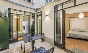 Un intérieur moderne avec une porte vitrée donnant sur une chambre, une petite table avec des chaises et une plante en pot.