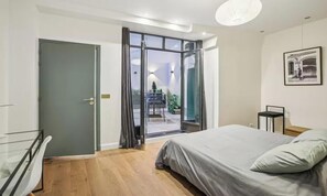Une chambre à coucher comprenant un lit, une table de chevet, un tableau encadré au mur et une porte-fenêtre coulissante donnant sur un espace extérieur.