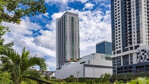 A modern high-rise building with a glass facade, surrounded by lush greenery and under a partly cloudy sky. - Miami Worldcenter Deluxe Stay! near Downtown (Miami)
