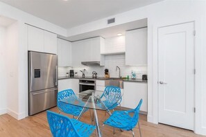 A modern kitchen with white cabinets, stainless steel appliances, and blue chairs around a glass table. - Miami Worldcenter Deluxe Stay! near Downtown (Miami)