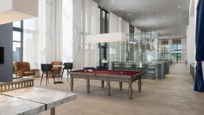 Een moderne hotel lobby met een biljarttafel, zachte zitplaatsen en een glazen vitrine.
