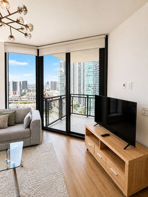 A modern living room with a large TV, a sofa, and a balcony with a city view. - Spacious Deluxe 2BR - Perfect near Bayfront Park  Family Stay (Miami)