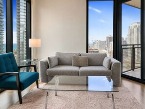 Ein modernes Wohnzimmer mit einem grauen Sofa, einem türkisfarbenen Sessel und einem Glastisch.
